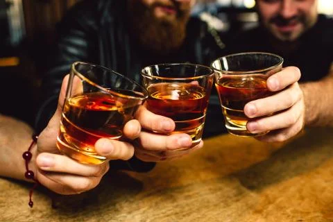 Cut view of three bearded young men holding glasses with rum together. They Stock-Fotos