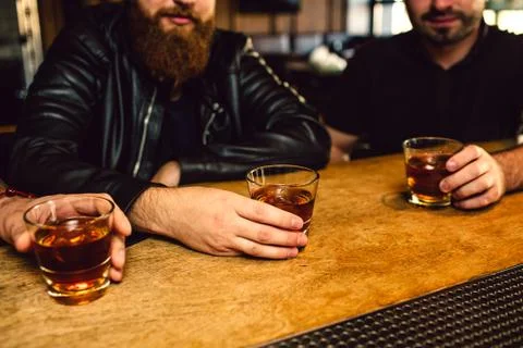 Cut view of three man sitting at bar counter. They hold glasses with rum. Guys Foto stock