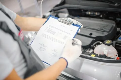 Cut view of worker stands at opened body of car and holds documents. He shows Foto stock