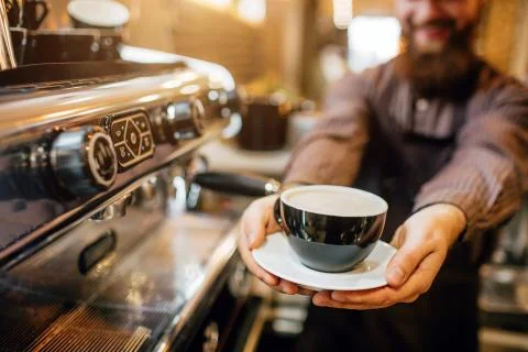 Cut view of young bearded man holding cup of coffee in hands. He stand in 写真素材