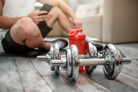 Cut view of young well-built man go in for sports in apartment. He sit on floor Stock Photos