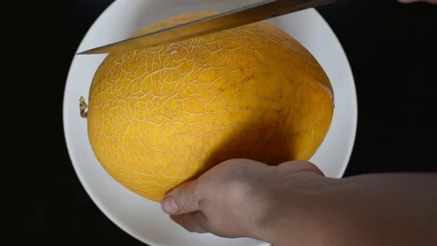 Cut the yellow melon on a white flat plate with a knife Stock Footage 96186754
