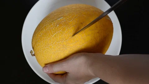 Cut the yellow melon on a white flat plate with a knife Stock Footage 96186845
