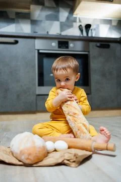 A cute 1-year-old boy is sitting in the kitchen and eating fresh bread. Child Foto stock