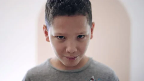 Cute 10 year old boy tries serious grumpy face but breaks expression to smile 스톡 동영상 194470730