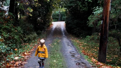 Cute 2 year old boy in yellow raincoat turns walks toward camera Stock Footage 82633748