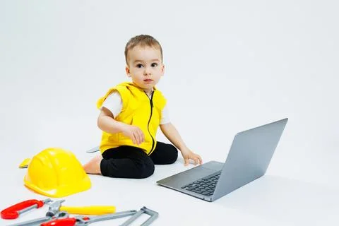 A cute 2-year-old boy is sitting at a digital laptop on a white background... Foto stock