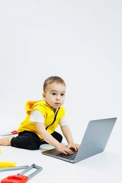 A cute 2-year-old boy is sitting at a digital laptop on a white background... Stockfoto's