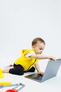 A cute 2-year-old boy is sitting at a digital laptop on a white background... Stockfoto's