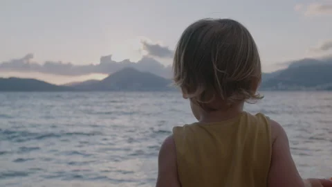 Cute 2-years boy with small carrot watching  at sea waves  at sunset Stock Footage 145348795