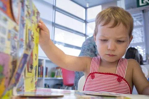 Cute 2 years boy turning a pop-up book page at library Stock Photos