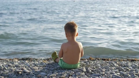 Cute 2 years old boy in green shorts playing with pebbles on Black sea beach Stock Footage 219593935