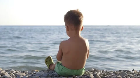 Cute 2 years old boy in green shorts playing with pebbles on Black sea beach Stock Footage 232565148