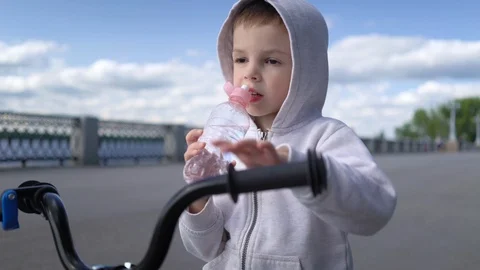 Cute 3 - 4 years boy child learning to ride first running balance bike and drink Stock Footage 113364071