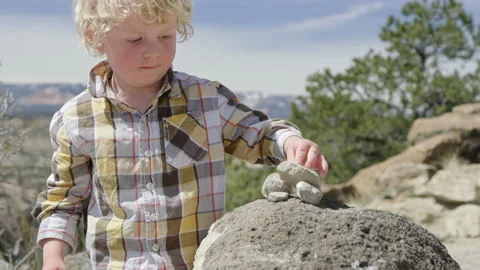 Cute 3 year old boy stacks small rocks on top of large rock, Escalante Utah Stock Footage 248581442