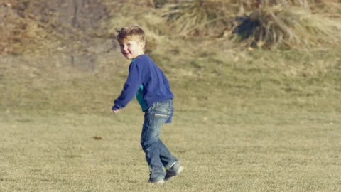 Cute 4 year old boy in blue green sweater runs away, turns and smiles, telephoto Stock-Footage 242191734