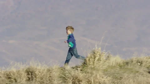 Cute 4 year old boy in sweater runs down hill, filmed with 800mm telephoto Stock-Footage 242191738
