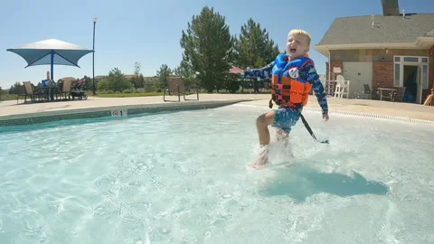 Cute 4 year old boy with life jacket runs in shallow end of pool while splashing Stock Footage 248080965
