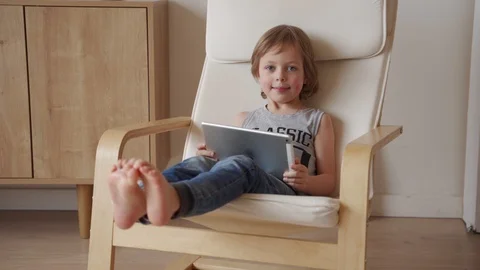 Cute 5 year caucasian boy sit in armchar and use tablet at light room Video stock 104224249