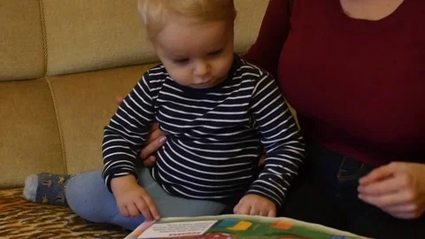 Cute 9-10 months old baby boy looks pictures in the book, mother turning page Stock Footage 82571362