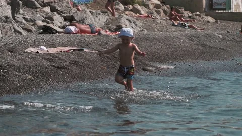 Cute active baby boy, walking and splashing in the water on the seashore in slow Stock Footage 182320777