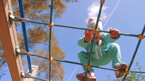 Cute active child climbs and crawls on horizontal rope wall on playground Stock Footage 137536337