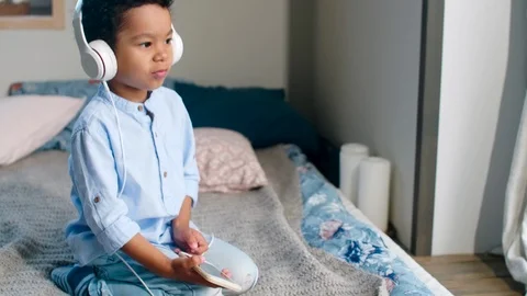 Cute African Boy Sitting on Bed and Listening to Music on Smartphone 스톡 동영상 101042253