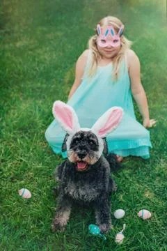 Cute Airedale Terrier dog in Easter bunny ears and little girl in bunny mask on Stock Photos