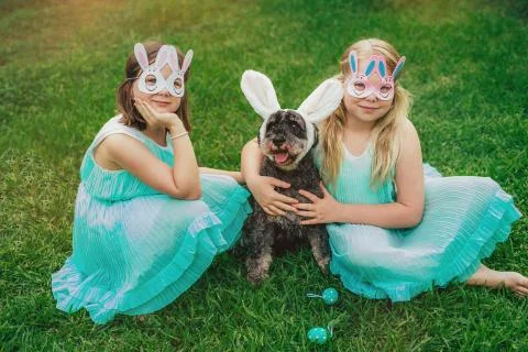 Cute Airedale Terrier dog in Easter bunny ears and little girls in bunny masks Stock Photos