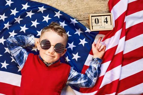 Cute and cheerful guy lying on a wooden background next to the American flag  Stock Photos