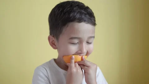 Cute asian boy eats a piece of orange on colour background Stock Footage 195038351