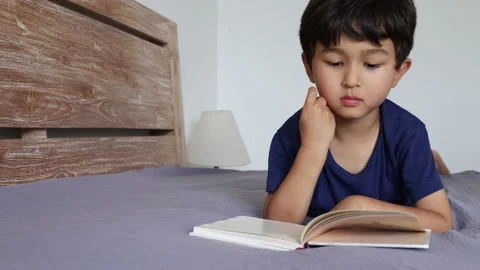 Cute asian boy reading a book on bed Stock Footage 162012012
