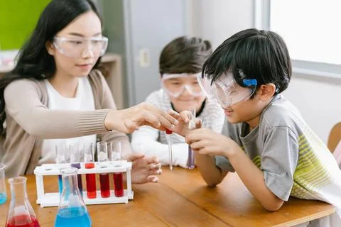 Cute Asian elementary schoolboy doing science while classmates looking his in Stock Photos