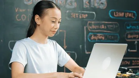 Cute asian girl programing system by using laptop at blackboard. Edification. 库存照片