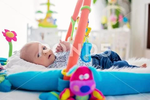 Cute baby boy on colorful gym, playing with hanging toys at home Stock Photos