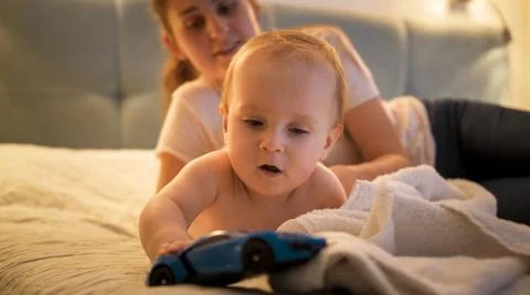 Cute baby boy crawling on bed and playing with toy car at night. Concept of Foto stock