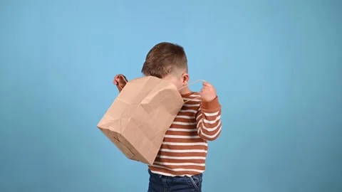 Cute baby boy looking inside paper bag on blue background. Shopping concept. Stock Footage 214343918
