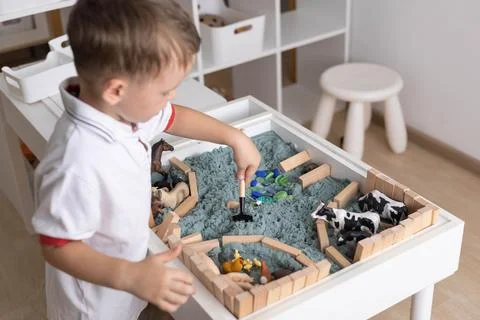 Cute baby boy playing sensory box kinetic sand table with farm animals Stock Photos