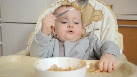 Baby boy in high chair eating pureed food with spoon - Stock Image