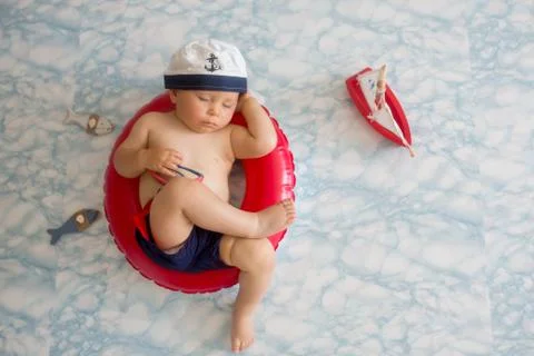 Cute baby boy sleeping on a tiny inflatable swim ring,  wearing swimsuit shor Stock Photos