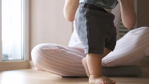 Cute baby doing the first steps and falls in slow motion at home near his mother Video stock 126491707