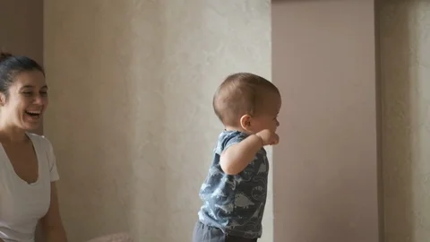 Cute baby doing the first steps and falls in slow motion at home near his mother Stock Footage 126493519