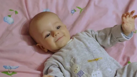 A cute baby lies on his back, smiling cheerfully and waving his arms. Vídeo Stock 192947853
