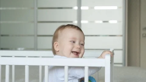 Cute baby in light clothes laughs in a crib in a bright room Stock Footage 73645129