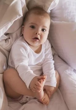 Cute baby is lying in bed holding his legs Stock Photos