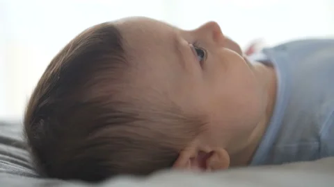 Cute baby lying on the bed, looking around, smiling. Side view, close-up shot Stock Footage 107747625