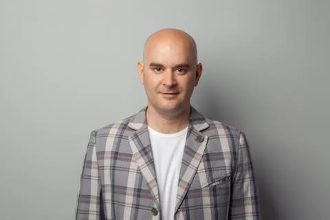 Cute bald man in a jacket and t-shirt shows against a gray wall Stock Photos
