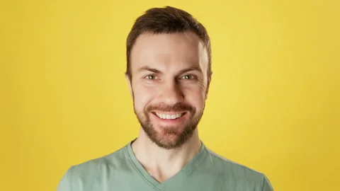 Cute bearded man smiling and looking at camera over yellow background. Stock Footage 222972898