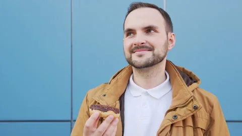 Cute bearded man sniffs a chocolate doughnut and admires its aroma. Video stock 135420910
