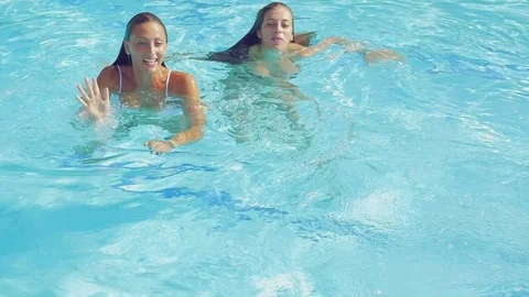 Cute beautiful girls inside pool waving saying hello to camera slow motion cl Stock Footage 78440123